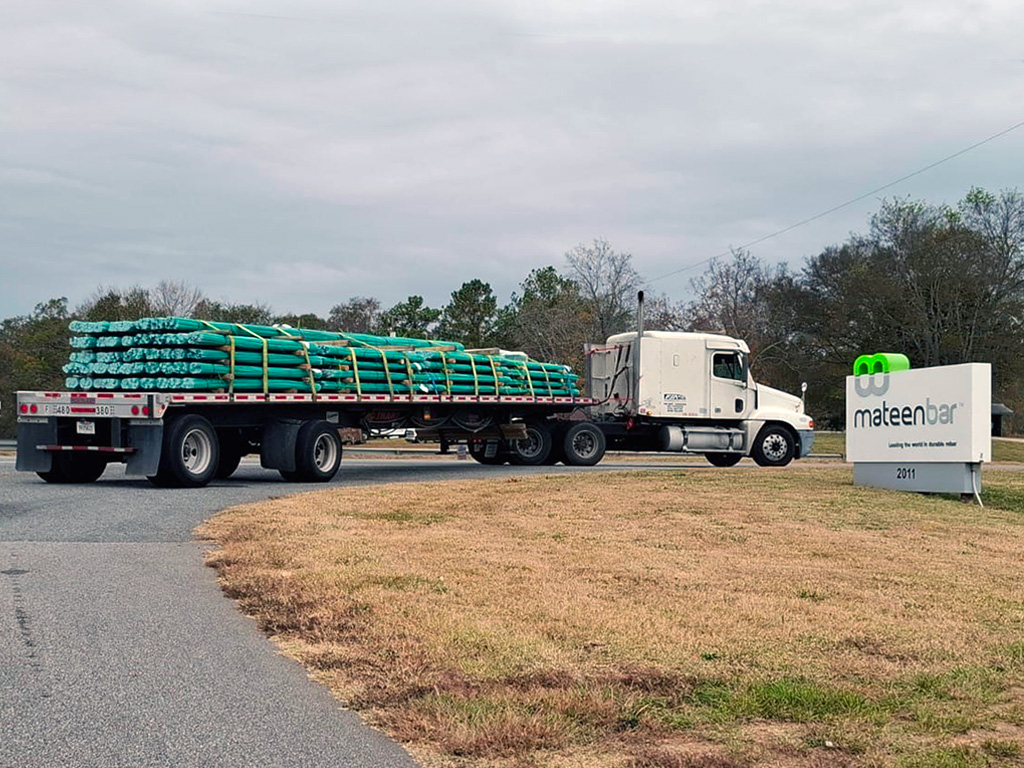 An 18-wheeler entering the Mateenbar Facility with bundles of fiberglass rebar, followed by a motorcyclist closely behind.