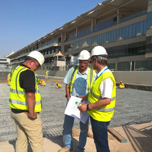 Three male construction workers talking in front of the Yas Island F1 Racetrack project.