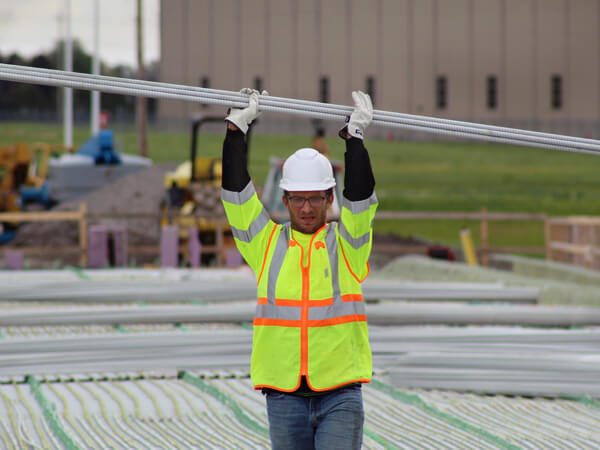 A construction worker wearing glasses holding Mateenbar60 GFRP above his head on a job site.