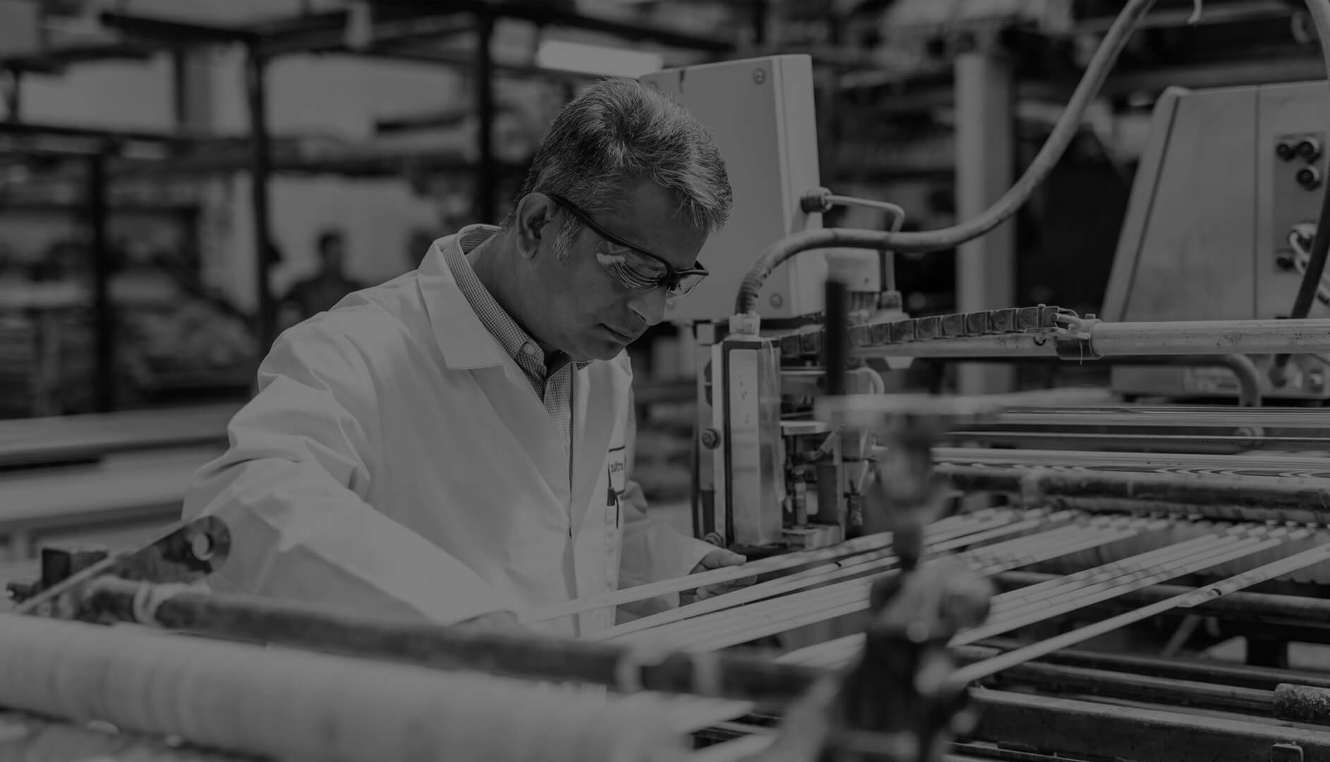 An engineer in a lab coat wearing safety glasses working on fiberglass rebar in a production facility