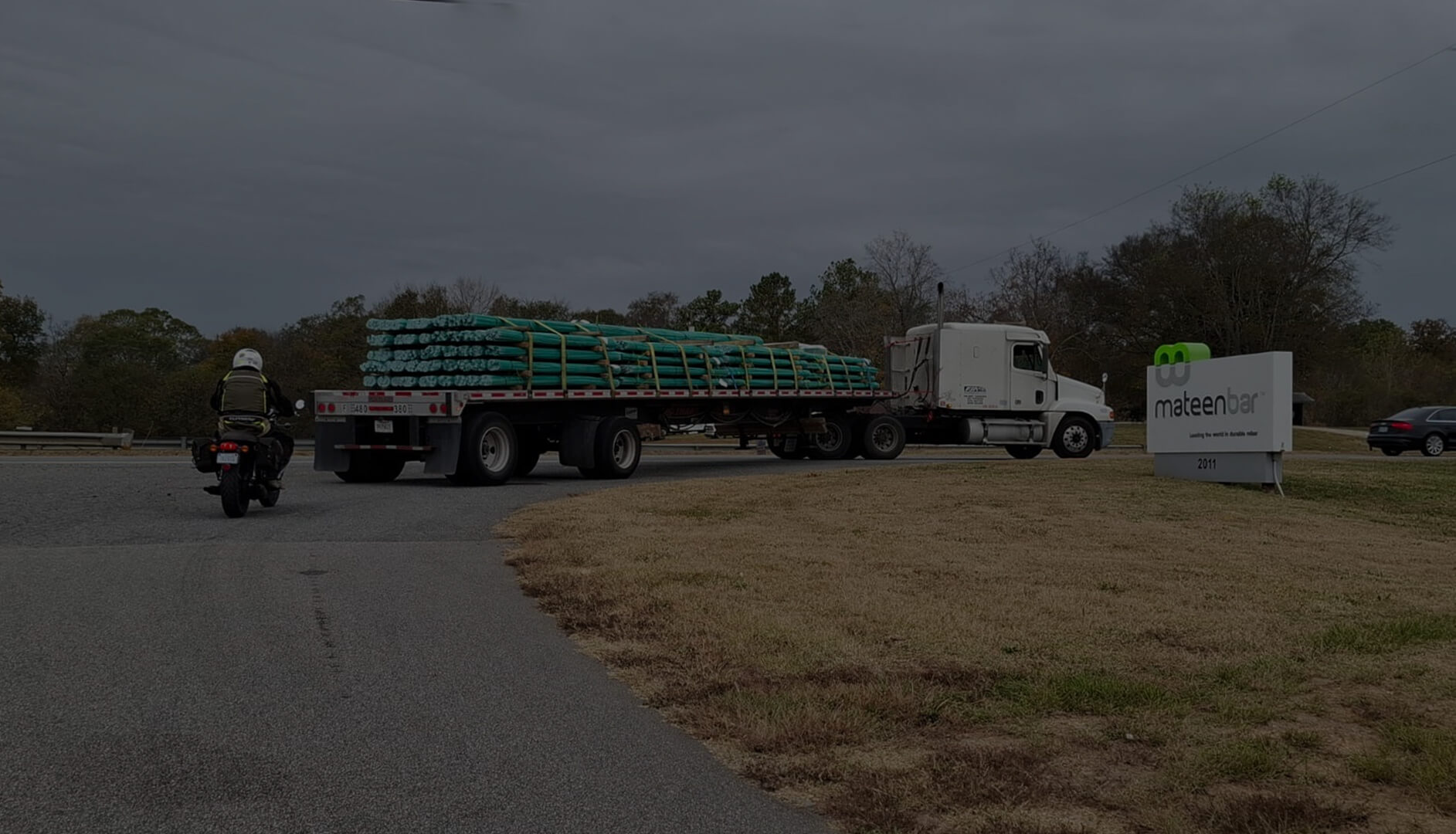 An 18-wheeler hauling bundles of fiberglass rebar heading into Mateenbar's production facility with a motorcyclist following behind.