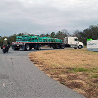 An 18-wheeler entering the Mateenbar Facility with bundles of fiberglass rebar, followed by a motorcyclist closely behind.