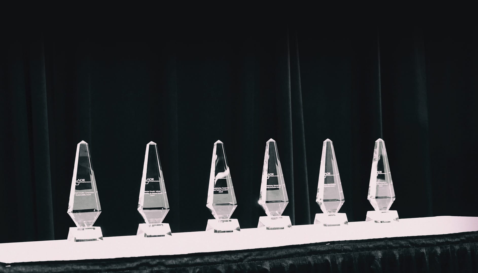 Six trophies lined up on a table in a dimly lit room