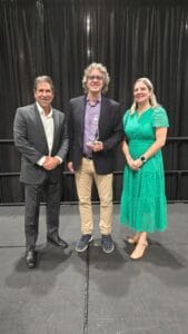 A woman and two men standing and posing for a picture, one man holding a trophy.