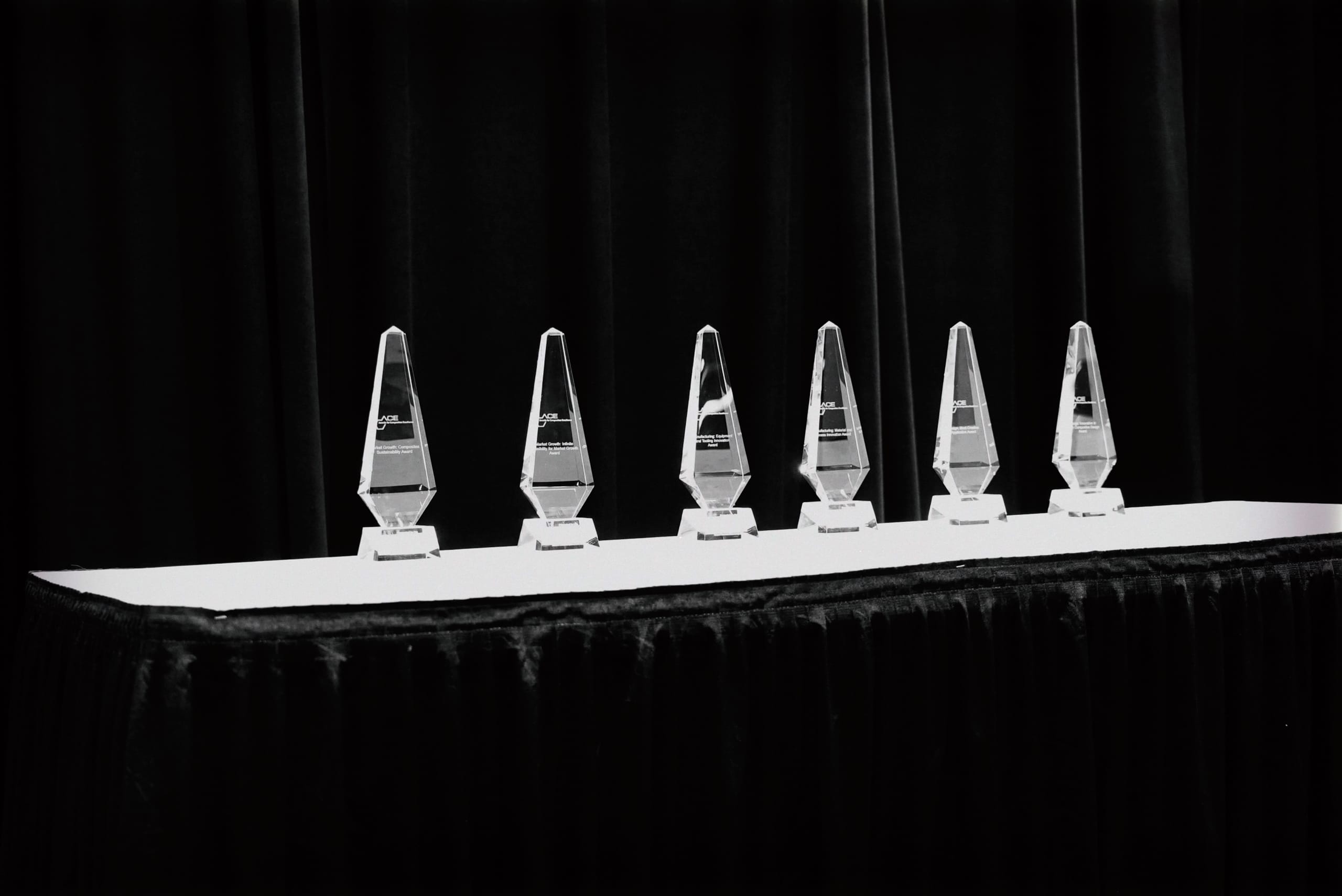 Six trophies lined up on a table in a dimly lit room